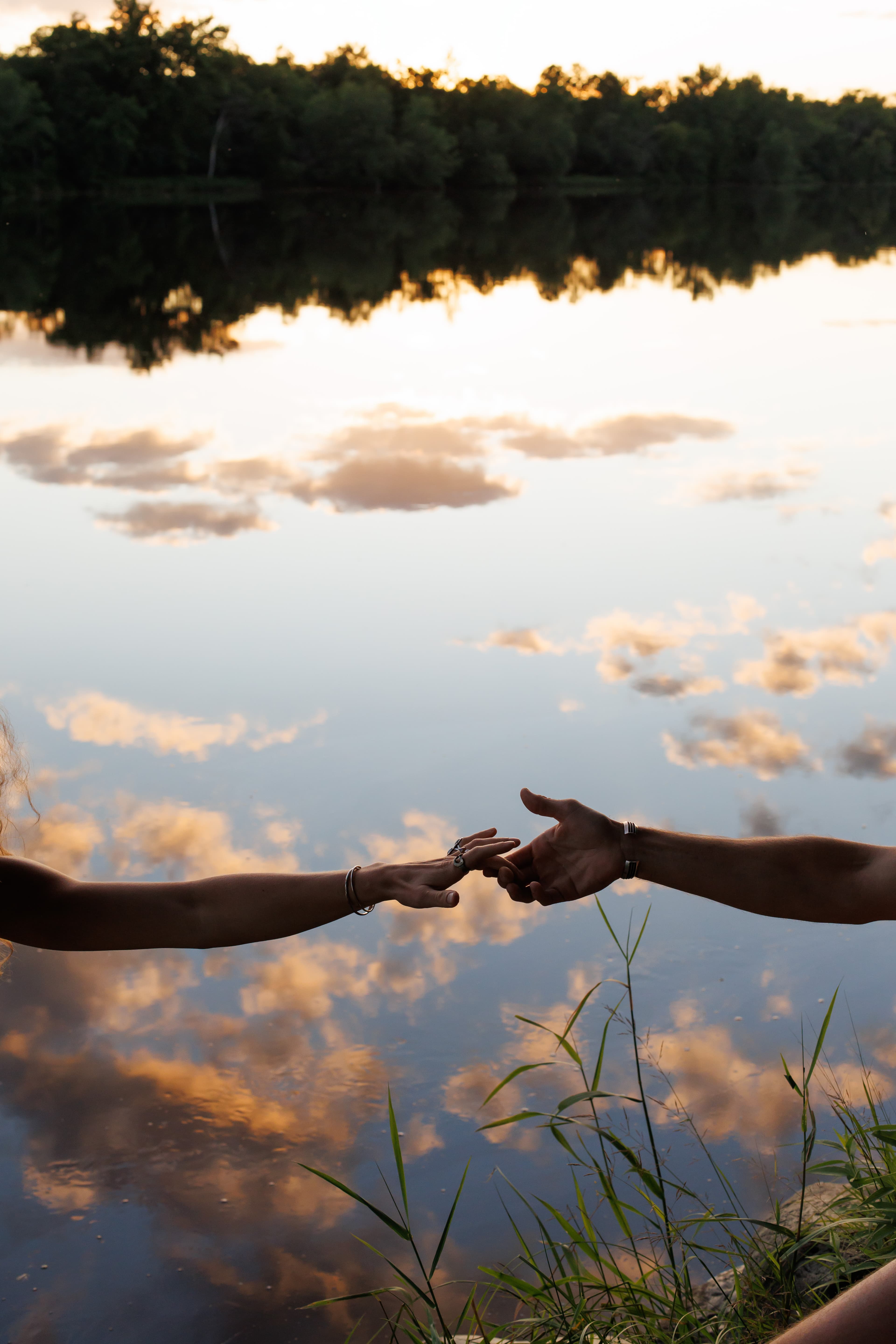 Couple holding hands with sunset lake reflection - romantic connection moment